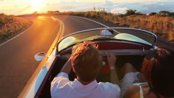 Pareja feliz conduciendo un coche convertible clásico en la puesta del sol en Country Road — Vídeo de stock