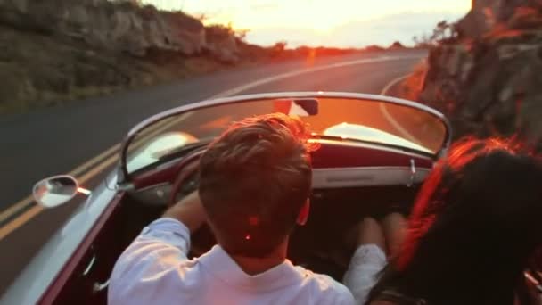 Pareja feliz conduciendo un coche convertible clásico en la puesta del sol en Country Road — Vídeos de Stock