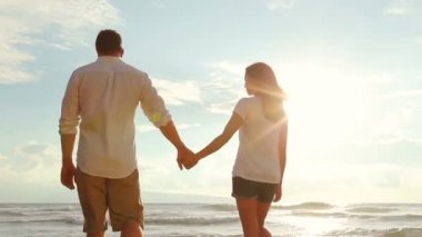 Güzel genç çift elele batımında sahilde yürüyüş