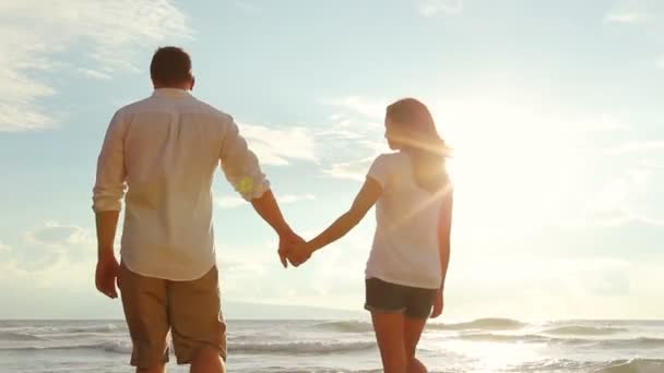 Hermosa pareja joven caminando en la playa sosteniendo las manos al atardecer — Vídeos de Stock