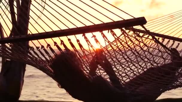 Young Woman with Blonde Hair Using Mobile Smart Phone while Relaxing in a Hammock Between Palm Trees at Sunset in Hawaii — Stock video