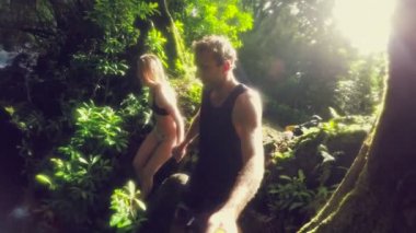 Young Adventure Couple Jumps Holding Hands off Cliff Into Water. Lush Green Jungle Waterfall.