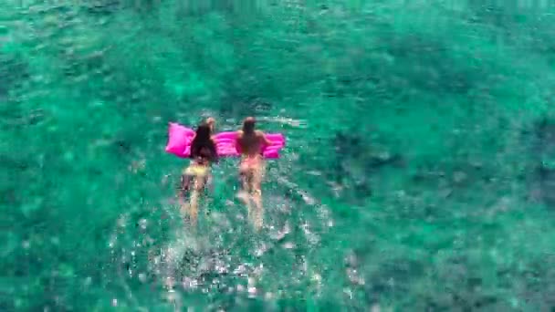 Vackra unga kvinnor i bikini svävar på rosa uppblåsbar flotte i kristall hav i Hawaii. — Stockvideo