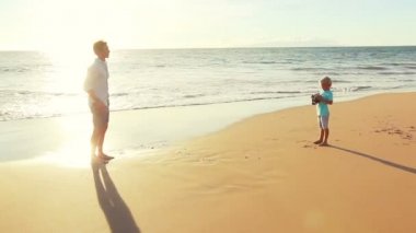 Baba ve oğul birlikte gün batımında sahilde oynarken.