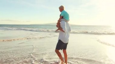 Baba oğlu batımında sahilde yürüyüş omuzlarında taşır.