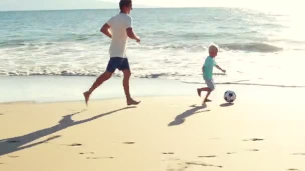 Vader en zoon te voetballen samen op het strand bij zonsondergang. — Stockvideo