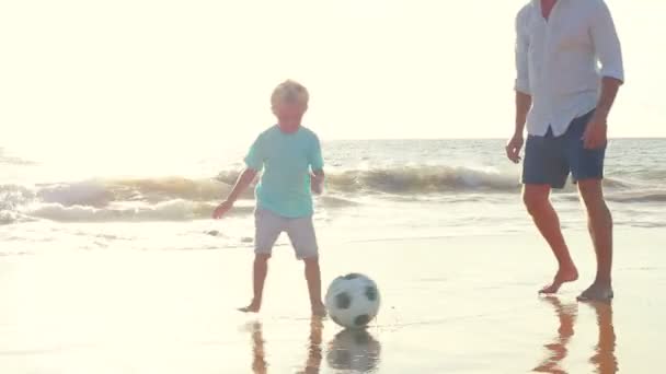 Ojciec i syn razem gra piłka nożna na plaży o zachodzie słońca. — Wideo stockowe