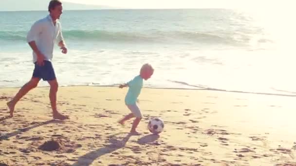 Otec a syn spolu hrají fotbal na pláži při západu slunce.