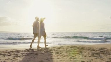 Gün batımı Yavaş Hareket'te Lüks Plajda Yürüyüş. Yaşlı Çift Hands Hold and Walks Down Beach At Sunset Onların Ayakları Isloldu