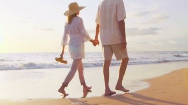 Tropik Plajda Gün Batımı Yürüyüşü. Yaşlı Çift Hands Hold and Walks Down Beach At Sunset Onların Ayakları Isloldu