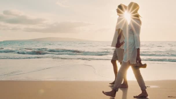 Sunset Walk op een luxe strand. Ouder echtpaar houdt handen en loopt langs het strand bij zonsondergang om hun voeten nat te krijgen — Stockvideo