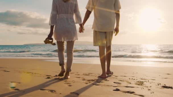 SLOW MOTION Coucher de soleil Promenade sur une plage de luxe. Couple plus âgé tient la main et descend la plage au coucher du soleil Obtenir leurs pieds humides — Video