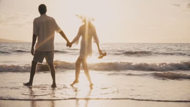 Sunset Walk op een luxe strand. Ouder echtpaar houdt handen en loopt langs het strand bij zonsondergang om hun voeten nat te krijgen — Stockvideo