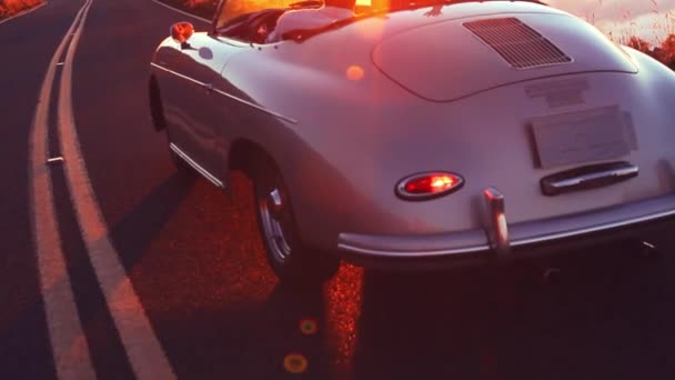 Ευτυχισμένο ζευγάρι οδήγηση σε επαρχιακό δρόμο στο ηλιοβασίλεμα στην κλασική εκλεκτής ποιότητας σπορ αυτοκίνητο — Αρχείο Βίντεο