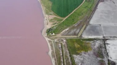 Kırmızı tuz gölünün ışıltılı su yüzeyi - stok videosu. Yüksek kalitede FullHD görüntüleri güneşli bir günde gökyüzüne karşı ünlü pembe gölün havadan çekilmiş görüntüleri, evlere doğru uçan insansız hava aracı, göl manzarası.