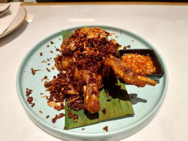 Ayam Goreng olarak bilinen gevrek ve lezzetli bir Endonezya yemeği, baharatlı sambal soslu muz yaprağının üzerinde servis edilir.