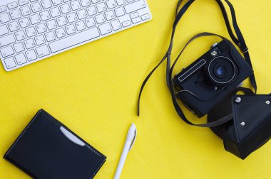 Background yellow flatlay keyboard camera in black leather case, pen, notebook with black cover. Travel concept, hobby, business, work, photographer. Background with cpy space. Template.