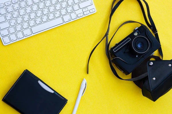 Background yellow flatlay keyboard camera in black leather case, pen, notebook with black cover. Travel concept, hobby, business, work, photographer. Background with cpy space. Template.