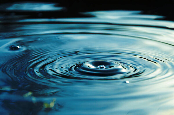 Circular waves and ripples in the water from a drop falling. Natural background blue water with circles and sky reflection.