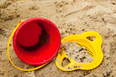 Unutulmuş oyuncaklar kum havuzunda kırmızı boş kova ve sarı elek kum ve çöp serpiştirilir..
