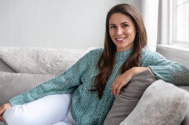 Evinde gülümseyen, rahat ve rahat bir şekilde kanepede oturan güzel bir genç kadının gizli bir hayat tarzı fotoğrafı.