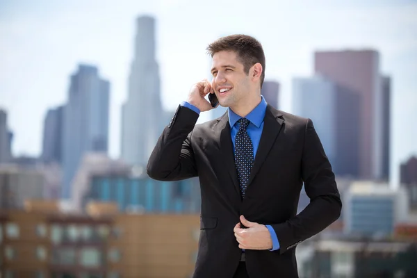 Schöner Geschäftsmann in der Innenstadt bei einem Handy-Anruf mit Skyline im Hintergrund — Stockfoto