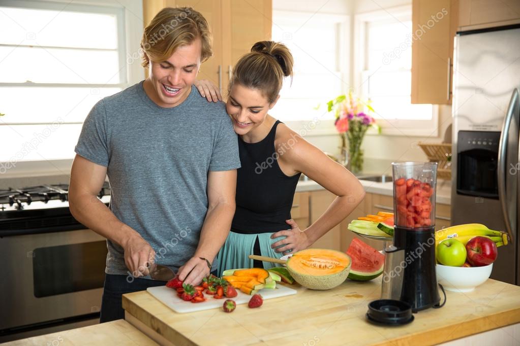 Attractive people in a kitchen making healthy low calorie smoothie lunch breakfast with fruits and veggies