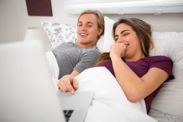 Couple in bed watching movies on computer laptop streaming video clips entertainment tv — 图库照片