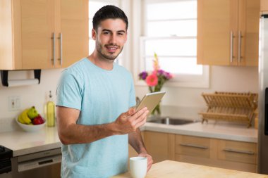 Man with smart tablet device reading the morning news with a  cup of coffee at home single male