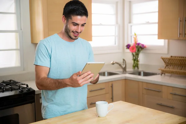 Bonito homem modelo masculino com tablet inteligente e xícara de café na cozinha casa redes sociais assistindo vídeos — Fotografia de Stock