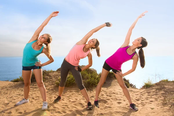 Stretching women outdoors on hike hill near ocean overlooking beach reach toward the sky — Stock Photo, Image