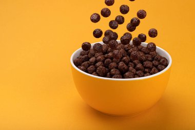 Çikolatalı mısır topları sarı arkaplanda, fotokopi alanı ve sağlıklı kahvaltı gevreği ile birlikte kaseye düşüyor.