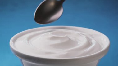 Mavi arka planda bir kase ekşi krema, kaşıklı Yunan yoğurdu.