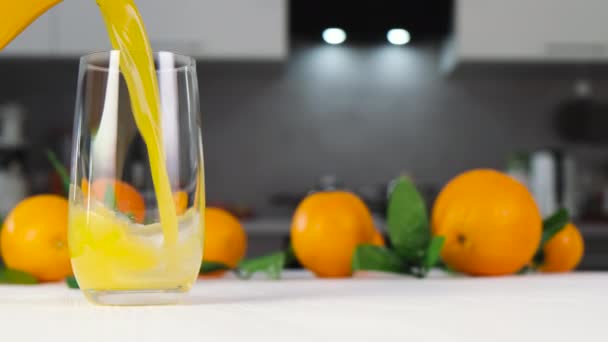 Апельсиновый сок наливается в стакан на белом столе — стоковое видео
