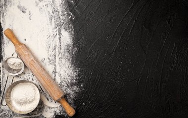 Siyah zemin üzerine serpiştirilmiş buğday unu ve ahşap merdane.