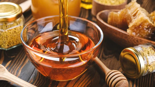 Honey in glass jar with honey dipper over wooden background with honeycomb and propolis, liquid sugar syrup, flower nectar