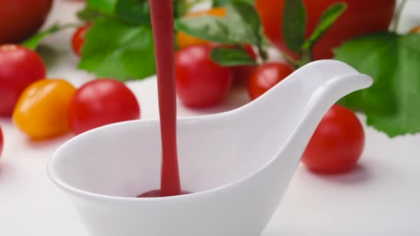 Pouring ketchup in bowl on white background with fresh tomatoes — Stock Video