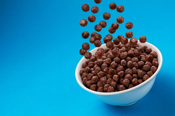 Bolinhas de milho de chocolate caindo em tigela sobre fundo azul — Fotografia de Stock