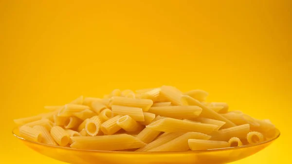 Crudo italiano penne rigate pasta sobre fondo de color amarillo con espacio de copia —  Fotos de Stock