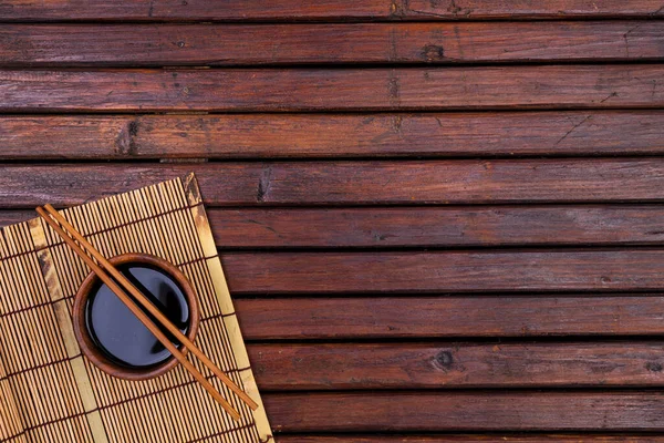 Antecedentes para sushi. Tapete de bambu, molho de soja, pauzinhos na mesa de madeira. Vista superior com espaço de cópia — Fotografia de Stock