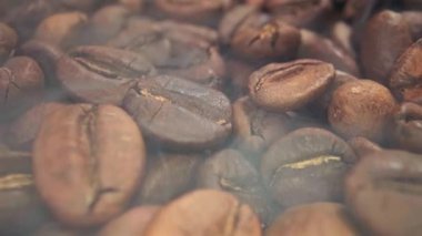 Kahve çekirdeklerini kavururken yavaş çekimde yükselen duman koyu arkaplanda yeni kavrulmuş tohumlar, üst görünümde.