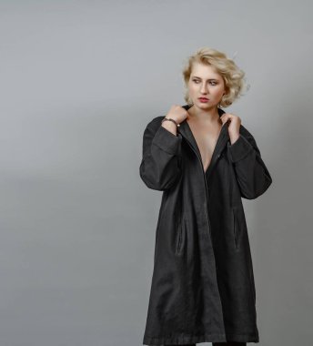 Gri arka planda siyah pelerinli, ince, çıplak sarışın kız.