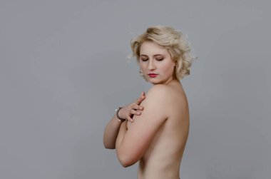 Kısa beyaz saçlı üstsüz manken kadın gri arka planda kameraya doğru dönüyor..