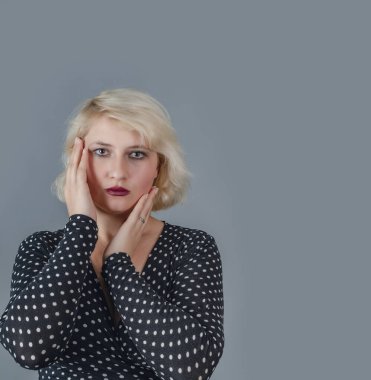 Stüdyoda noktalı elbiseyle poz veren güzel sarışın kız. Gri arkaplanda portre.