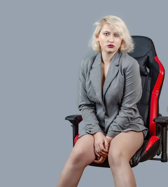 Gri Ceketli Genç Bir Kadın Gri Arka Planda Ofis Sandalyesinde — Stok fotoğraf
