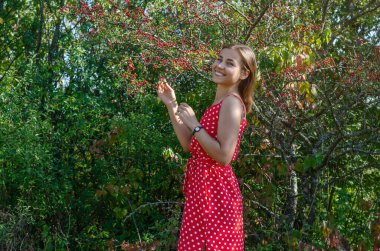 Kızıl dikenli böğürtlenli çalıların yanında genç bir kadın. Gülümse, doğal güzellik.