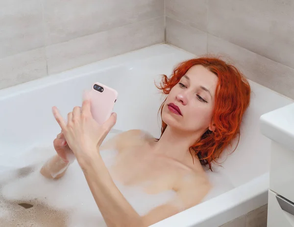 年轻女人躺在浴室里拿着电话 在电话上留言 在电话里说话 — 图库照片