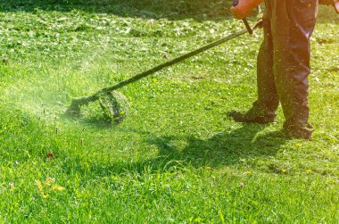 Koruyucu pantolonlu işçi çimenlikte çim biçme makinesiyle yeşil çim biçiyor..