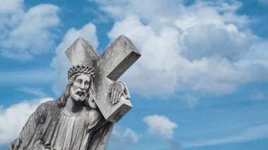 Çarmıhı taşıyan İsa 'nın taş heykeli. Bulutlardaki mavi gökyüzünün arka planında bir mezar taşı. Dini tarikat, kefaret, Hristiyanlık