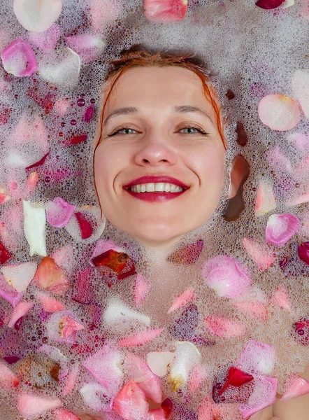 Pretty woman in the bathroom. Face over the water. Relaxation.  Rose petals in water